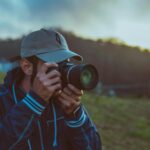 A man with a camera captures the serene outdoor landscape at sunset, highlighting a moment of focus and passion.